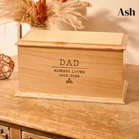 A wooden cremation urn for ashes. The cremation urn is rectangular and is made of ash. It is engraved with the words "Dad - Always Loved 1963 - 2023" and a small picture of a person sitting on a motorbike. 