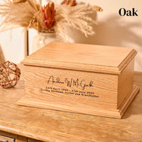 A wooden cremation urn. The urn is rectangular and is made of oak and has a personalised engraving which reads "Andrew W. McGrath - 14th April 1961 - 21st June 2023 - Loving Husband, Father and Grandfather"