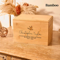 A wooden cremation urn. The urn is rectangular and made of bamboo wood. It has an engraving showing the outline of a dove in flight, carrying an olive branch in its beak. A personalised engraving underneath the dove reads "Christopher Taylor - A wonderful husband, father and grandpa. We miss you every day - 1971-2023"