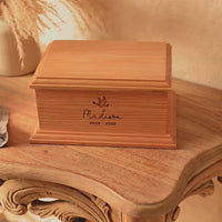 A personalised wooden cremation urn for a child sits on a wooden table. The urn is rectangular and is engraved on the front face with the name Madison. It is an urn for a stillborn baby, an urn for a child or an urn for a miscarriage.