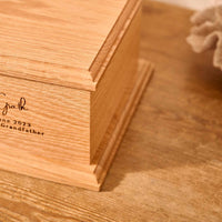 A close up of detail on a personalised cremation urn. The urn is rectangluar and is made of a light wood. The photograph is focused on bevelling detail around the corners and edges of the urn.