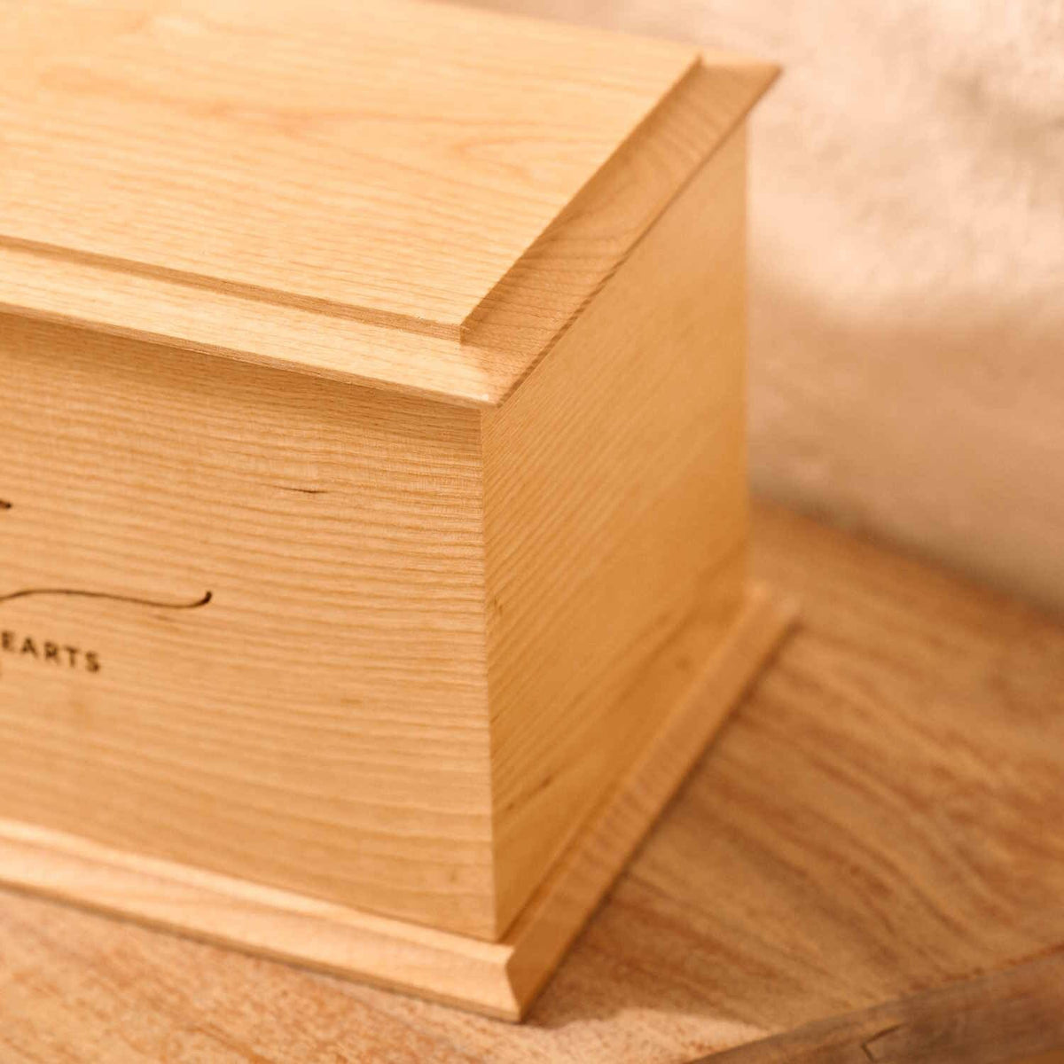 A close up of detail on a personalised cremation urn. The urn is rectangluar and is made of a light wood. The photograph is focused on bevelling detail around the top face of the urn.