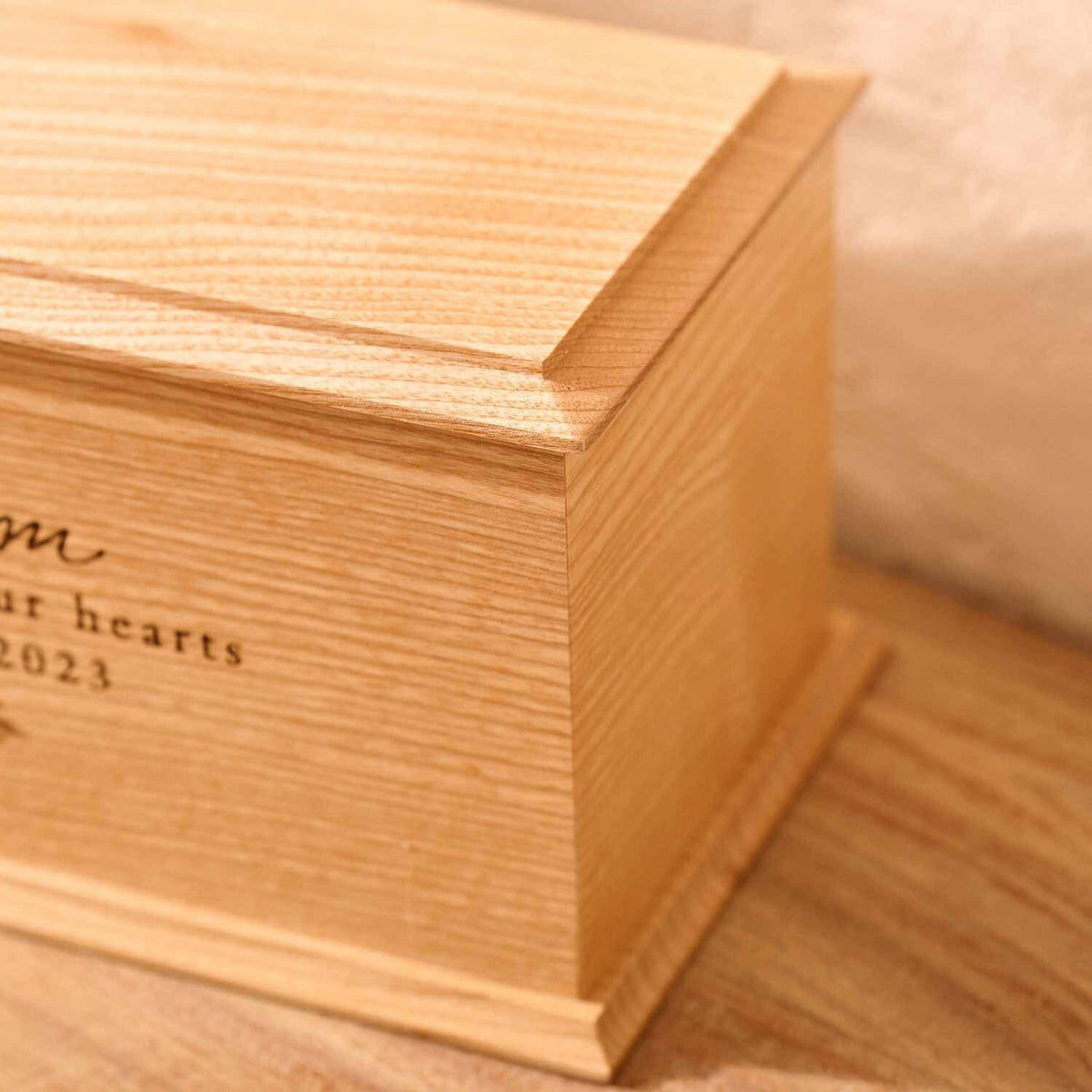 A close up of detail on a personalised cremation urn. The urn is rectangluar and is made of a light wood. The photograph is focused on bevelling detail around the top face of the urn.