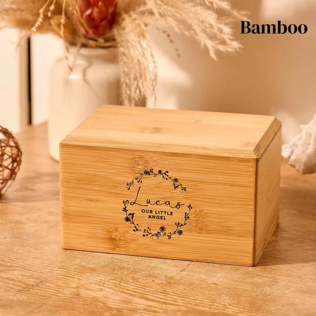 A wooden cremation urn for stillborn ashes. The cremation urn is rectangular and is made of bamboo. It is engraved with a wreath design, a name and a message. 