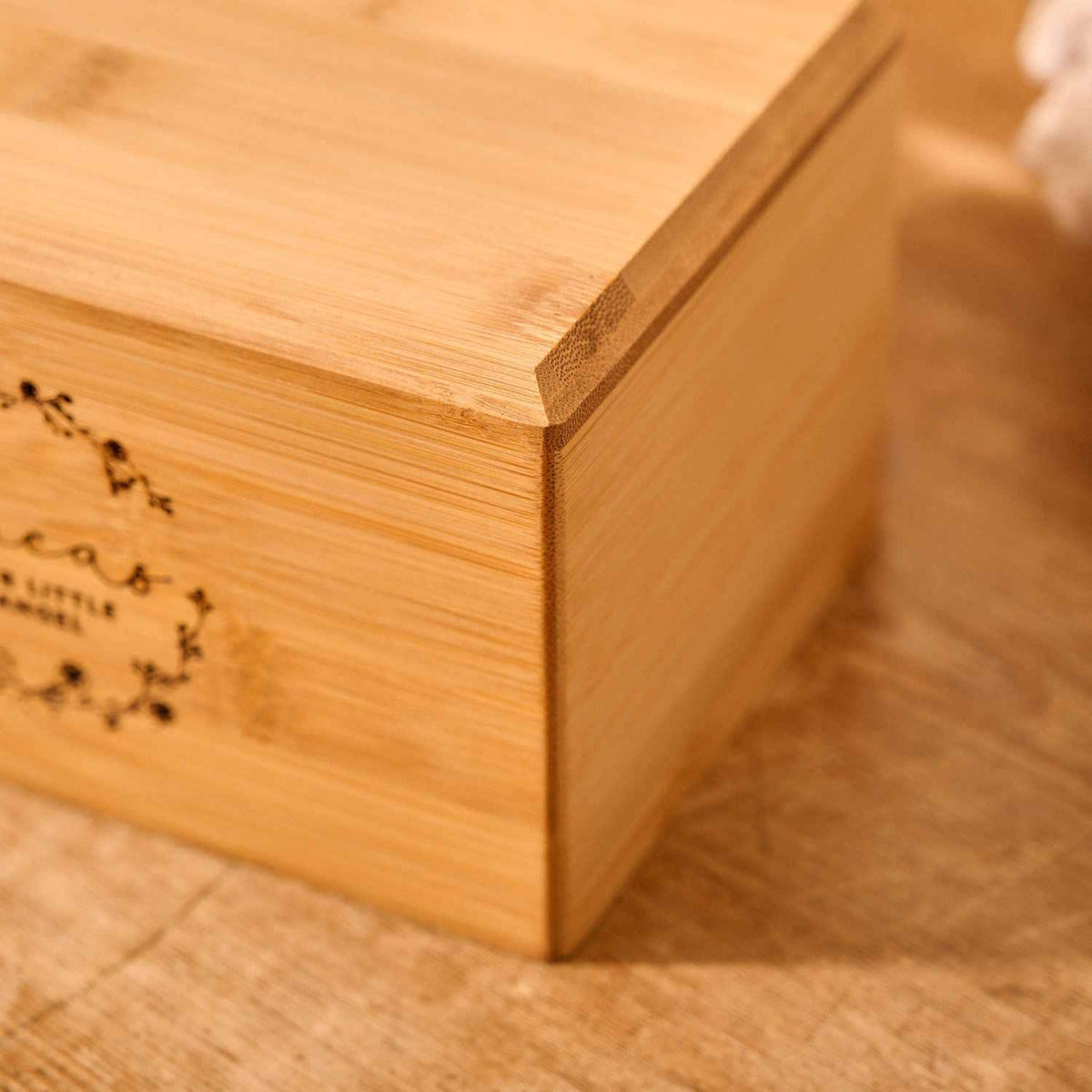 A close up of detail on a personalised cremation urn. The urn is rectangluar and is made of a light wood. The photograph is focused on bevelling detail around the top face of the urn. There is floral detail on the urn. It is an urn for a stillbirth or urn for a miscarriage.