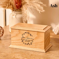 A wooden cremation urn for stillborn ashes. The cremation urn is rectangular and is made of ash. It is engraved with a wreath design, a name and a message. 