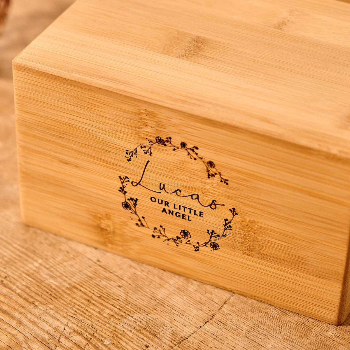 A personalised cremation urn for a child or stillborn. The urn is rectangular and is engraved on the front face with the words "Lucas - Our Little Angel". It is an urn for a stillborn baby, an urn for a child or an urn for a miscarriage. The text is encased with a floral wreath.