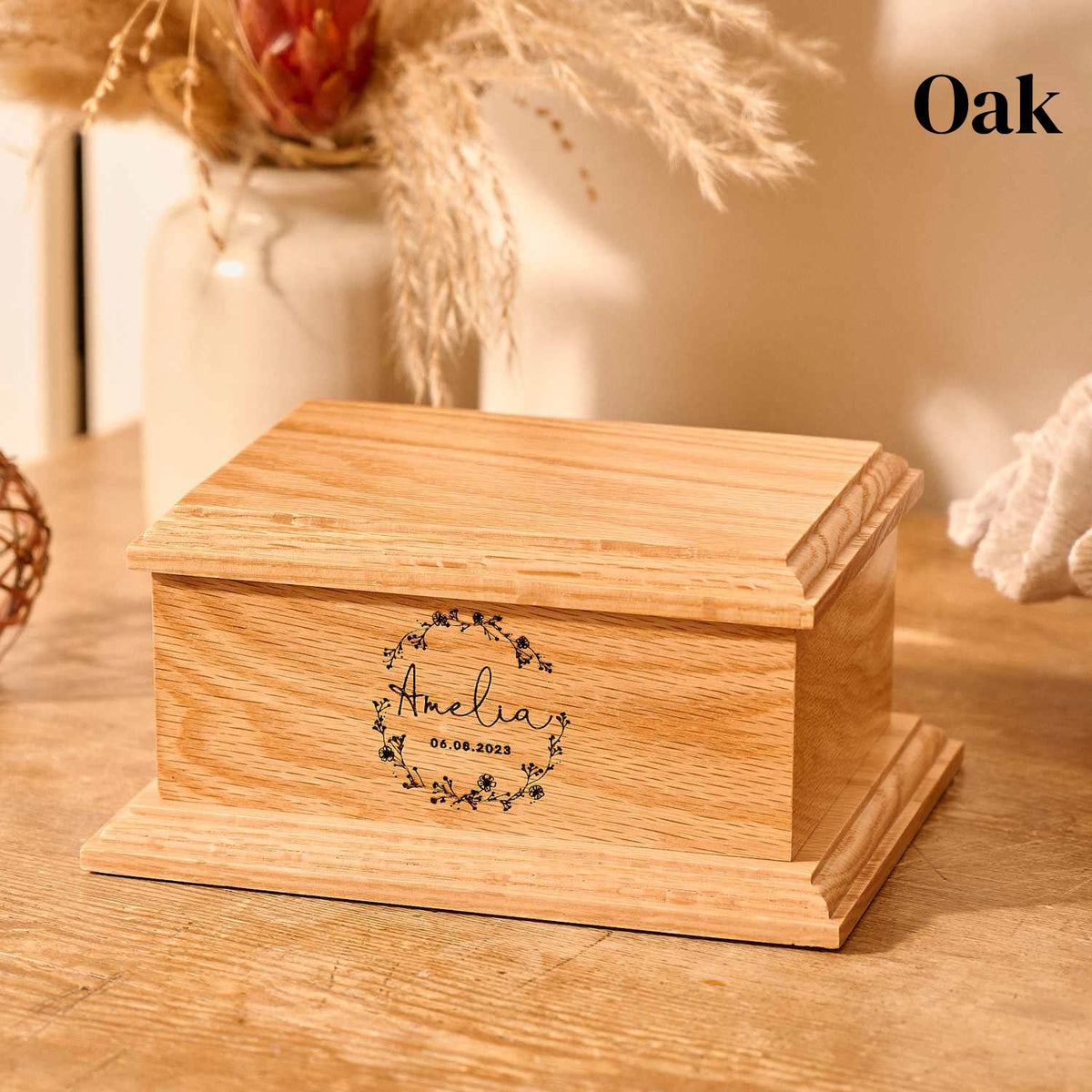 A wooden cremation urn for stillborn ashes. An oak casket for ashes. It is engraved with a wreath design, a name and a message. 