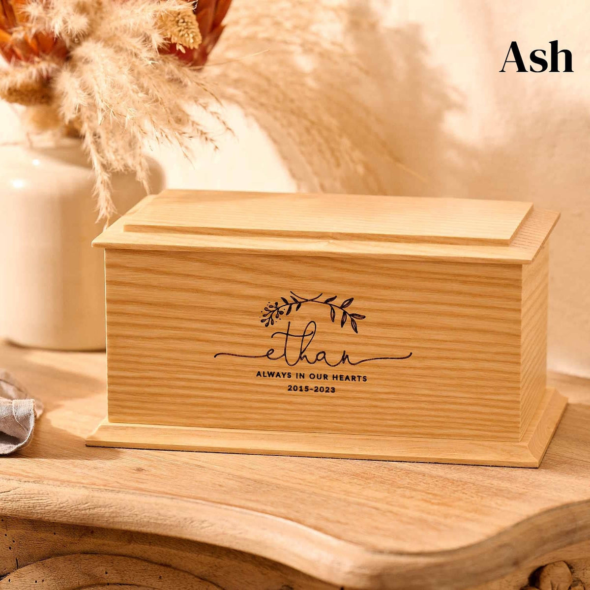 A personalised wooden cremation urn for a child sits on a wooden table. The urn is rectangular and is engraved on the front face with the name Ethan. It is an urn for a stillborn baby, an urn for a child or an urn for a miscarriage.