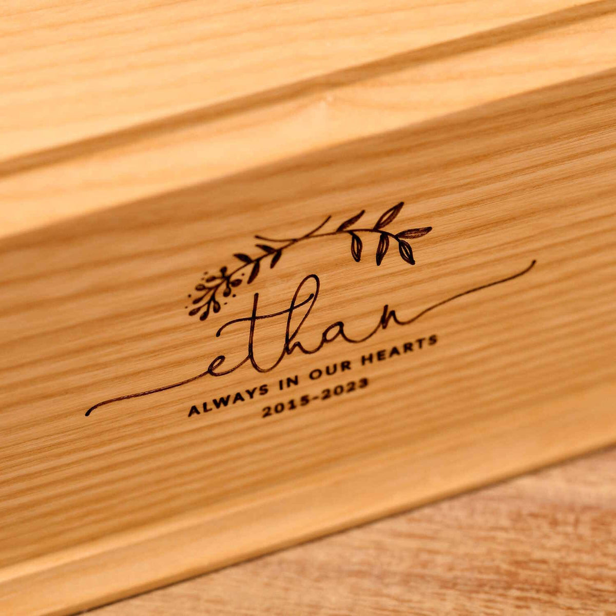 A personalised cremation urn for a child sits on a wooden table. The urn is rectangular and is engraved on the front face with the name Ethan. It is an urn for a stillborn baby, an urn for a boy, an urn for a girl or an urn for a miscarriage.