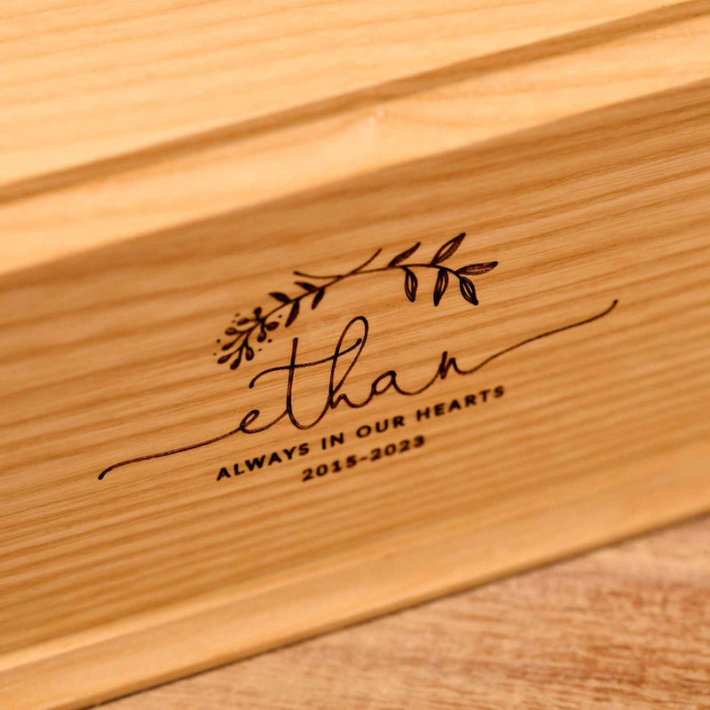 A personalised cremation urn for a child sits on a wooden table. The urn is rectangular and is engraved on the front face with the name Ethan. It is an urn for a stillborn baby, an urn for a boy, an urn for a girl or an urn for a miscarriage.