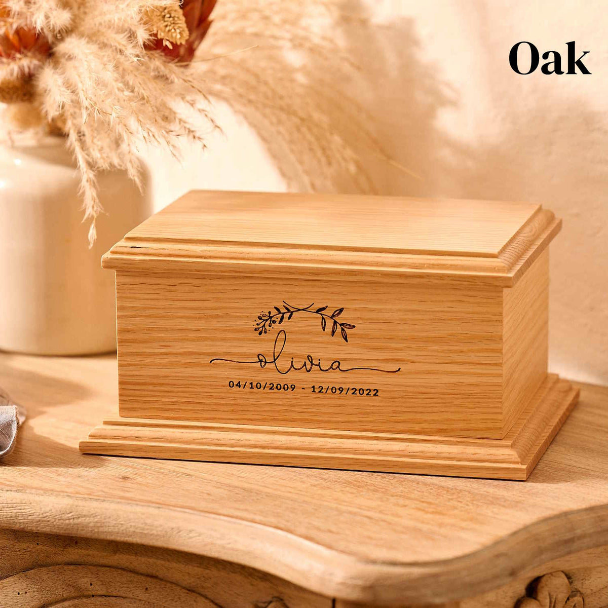 Wooden urn for a child sits on a table. The name Olivia is engraved over dates of birth and death.