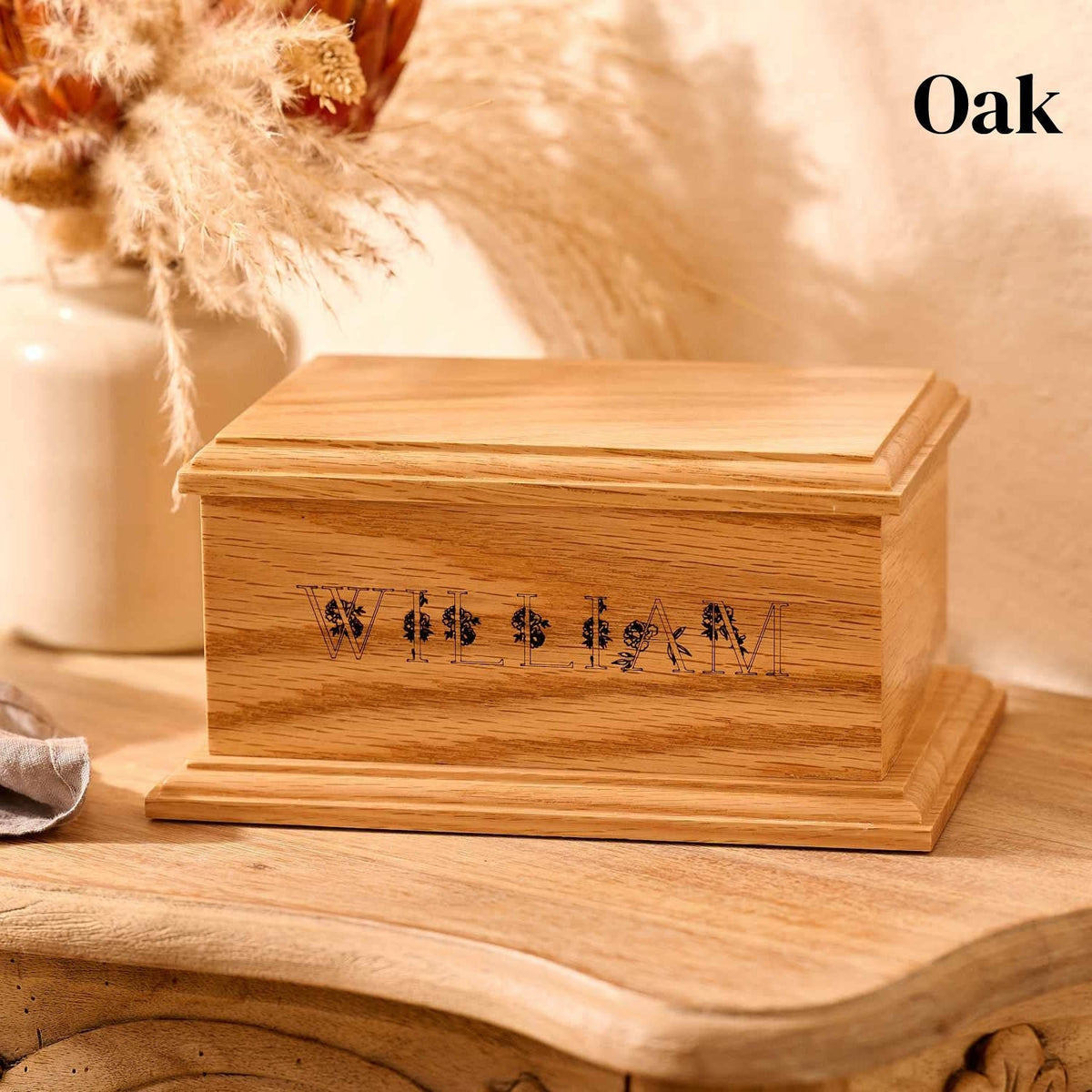 A personalised wooden cremation urn made of oak. The cremation urn has the name "william" on it, written in capital letters. The letters have a floral design.