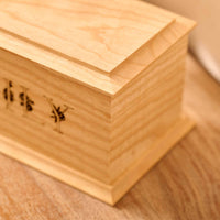 A close up of detail on a personalised cremation urn. The urn is rectangluar and is made of a light wood. The photograph is focused on bevelling detail around the top face of the urn.