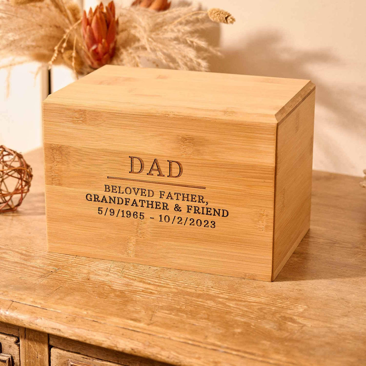 Dad's ashes sit in a wooden urn on a table. The cremation urn says "dad" on the front. This is an urn for cremation ashes.