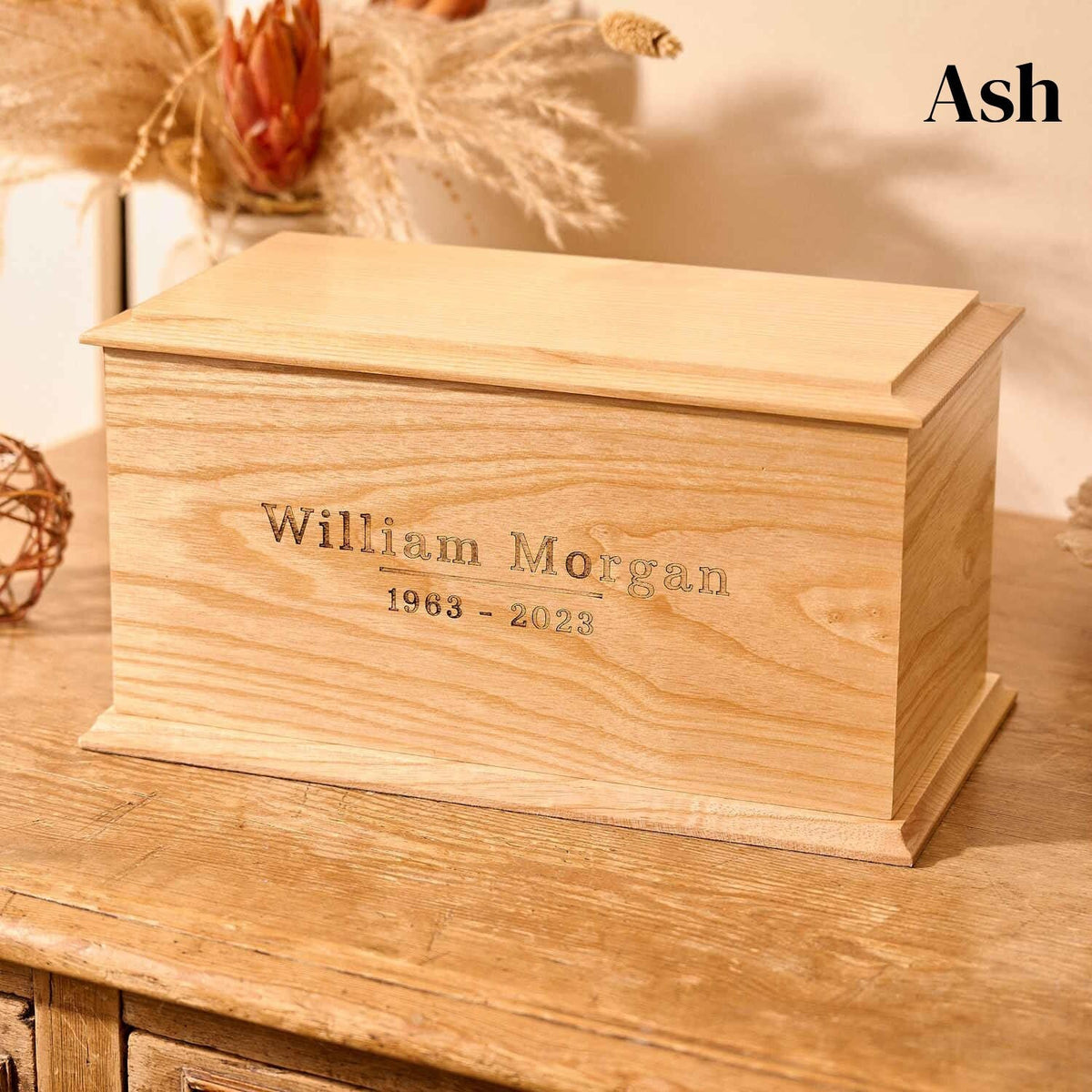 Engraved ash man's urn sits on a table. It is personalised and could be a woman's urn. The name William is on the front. It is an ash cremation urn.