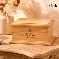 A personalised wooden cremation urn for a child sits on a wooden table. The urn is rectangular and is engraved on the front face with the name Madison. It is an urn for a stillborn baby, an urn for a child or an urn for a miscarriage.